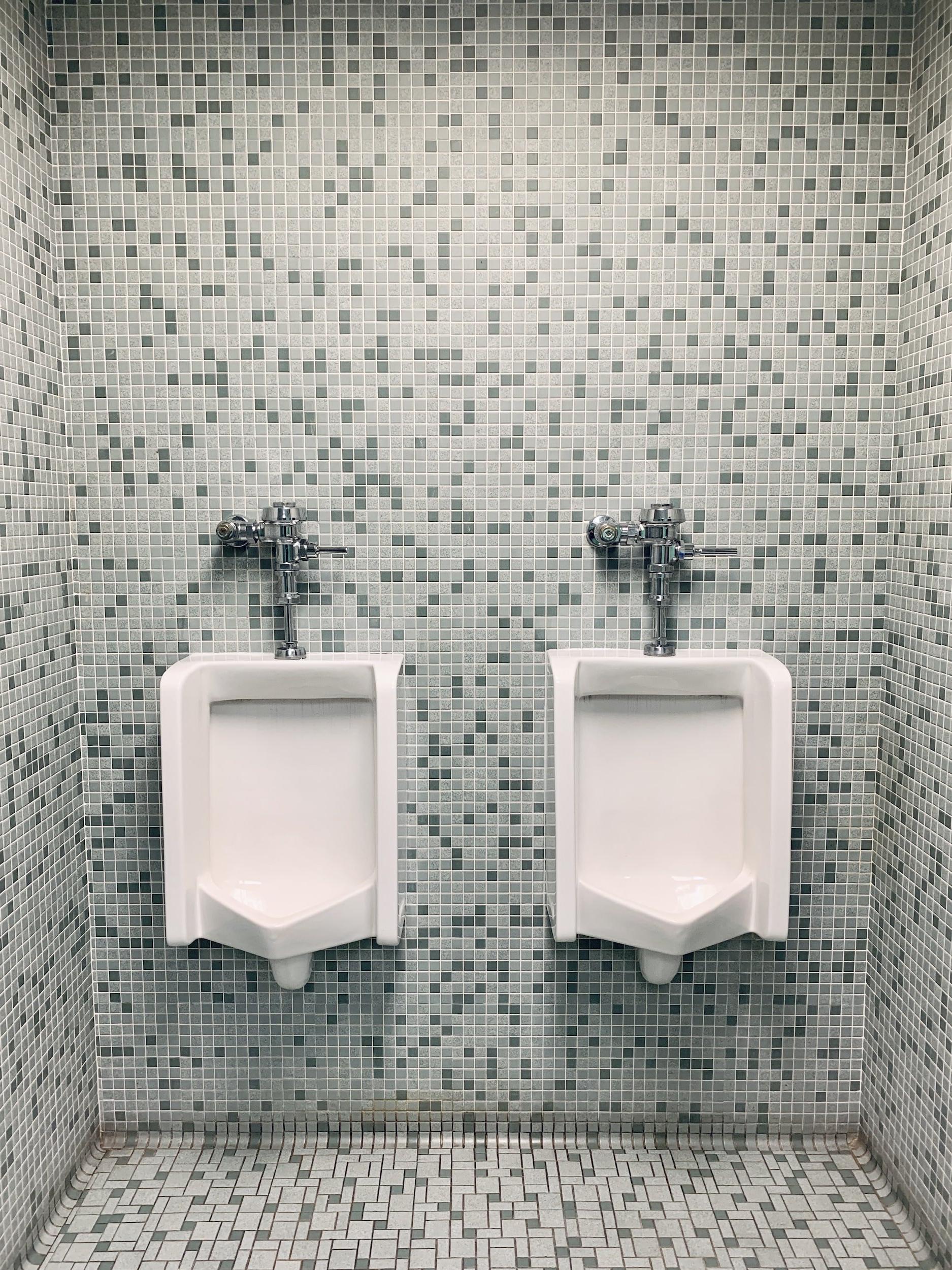 Two urinals on a blue tiled background.