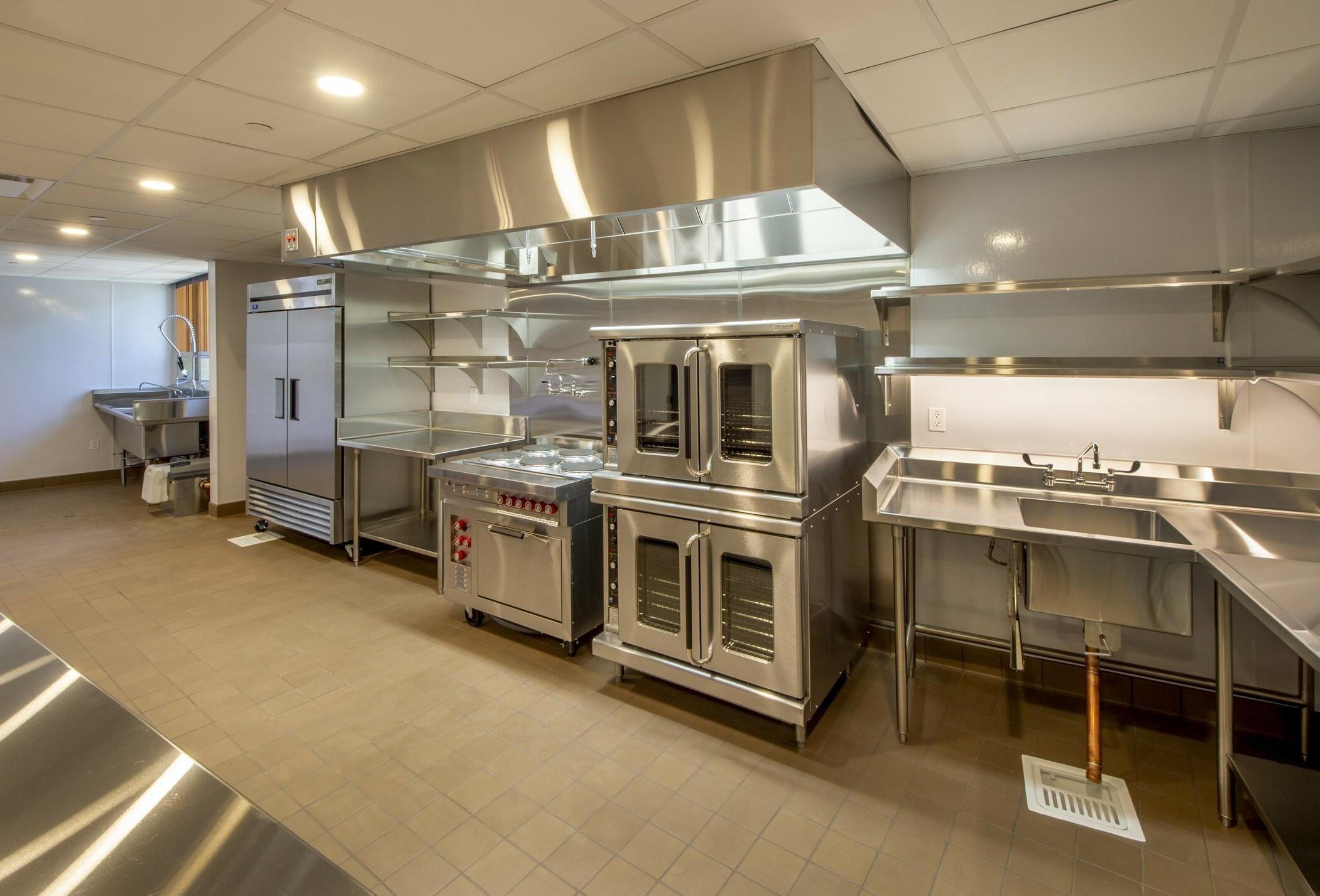 Commercial kitchen setting with ground drain, sink, oven, and refridgerator.