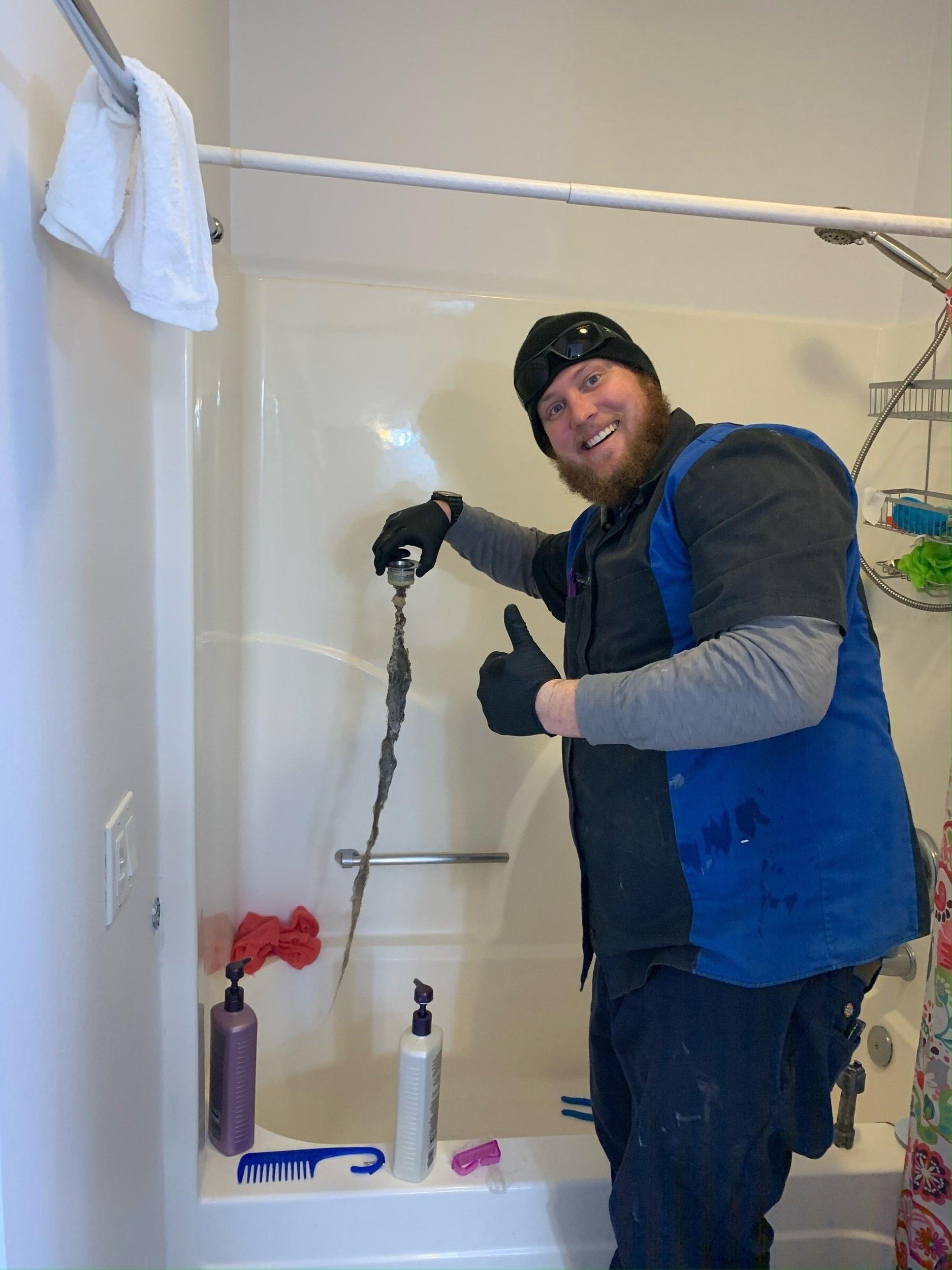 Renew plumbing employee holding a drain stopper with hair and debris attached to it while giving a thumbs up to the camera.